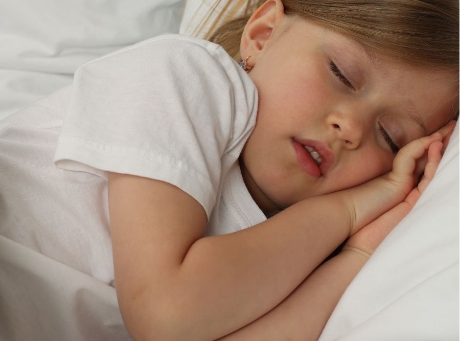 A young girl sleeping soundly on a white pillow with her mouth slightly open